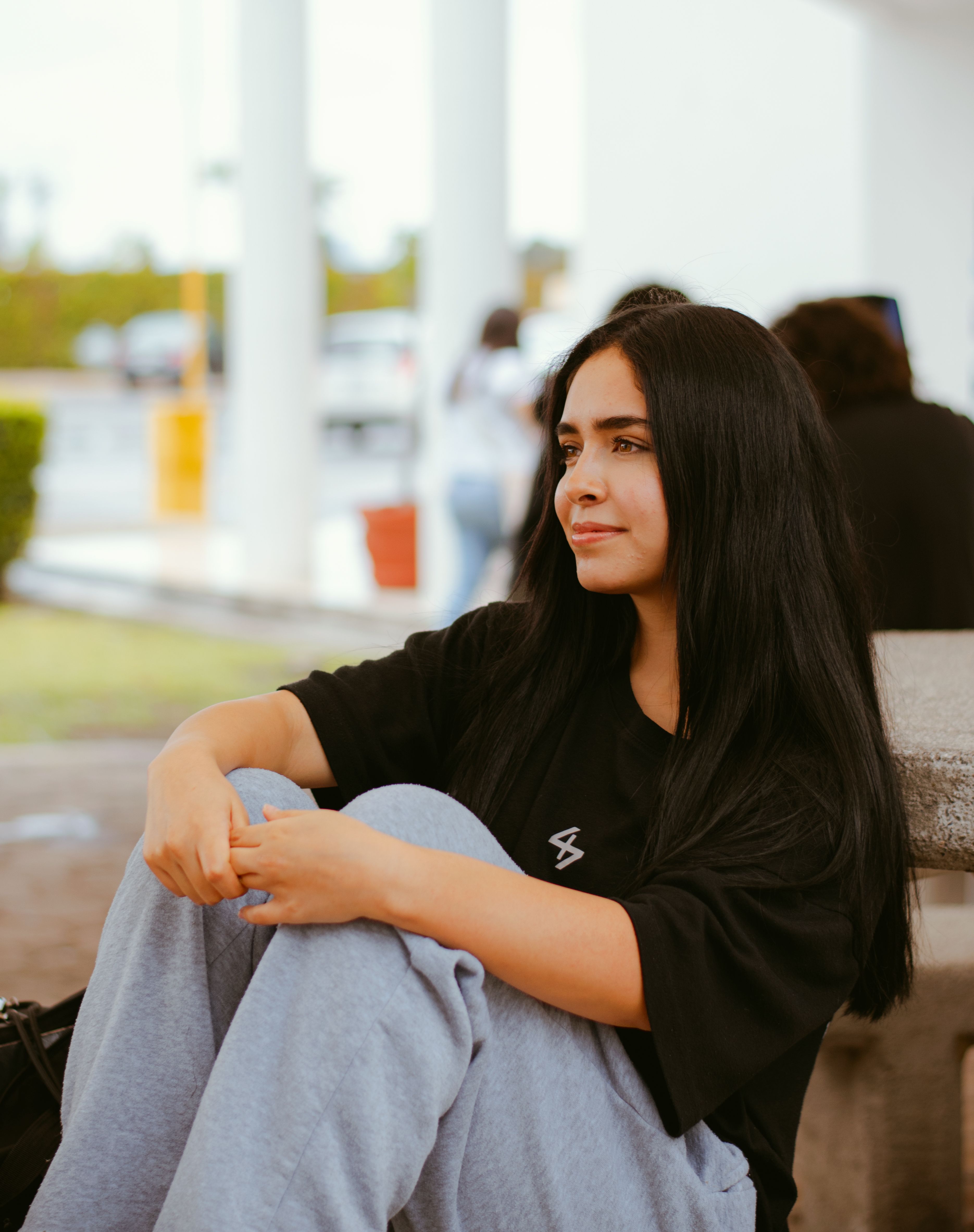 Young woman sitting outside, thoughtfully gazing into the distance, in comfortable casual clothing.