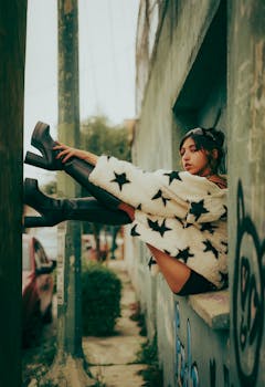 Stylish woman in star-patterned jacket and boots posing outdoors by graffiti wall.