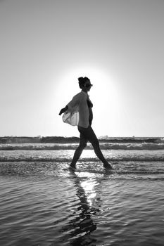 Silhouette of a woman walking along the beach with the sun setting behind her.