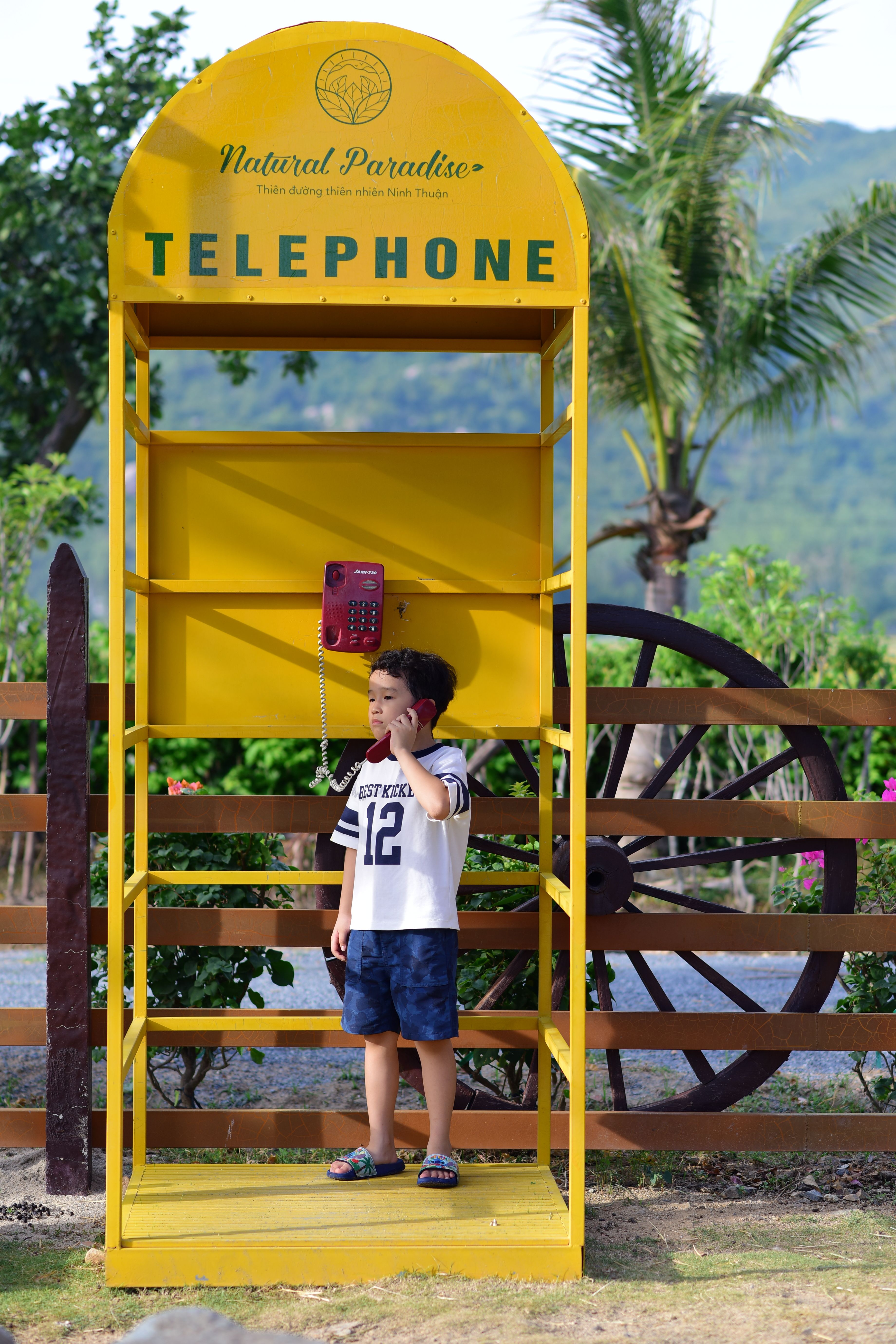 Child using retro yellow telephone booth outdoors · Free Stock Photo