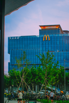 Cityscape at dusk with modern glass building and McDonald's logo, bicycles in foreground.