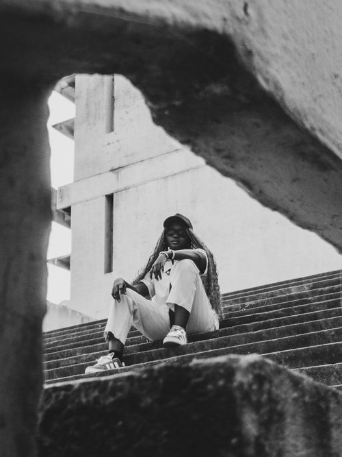 Free Black and white image of a person sitting on steps in an urban setting, showcasing modern fashion. Stock Photo