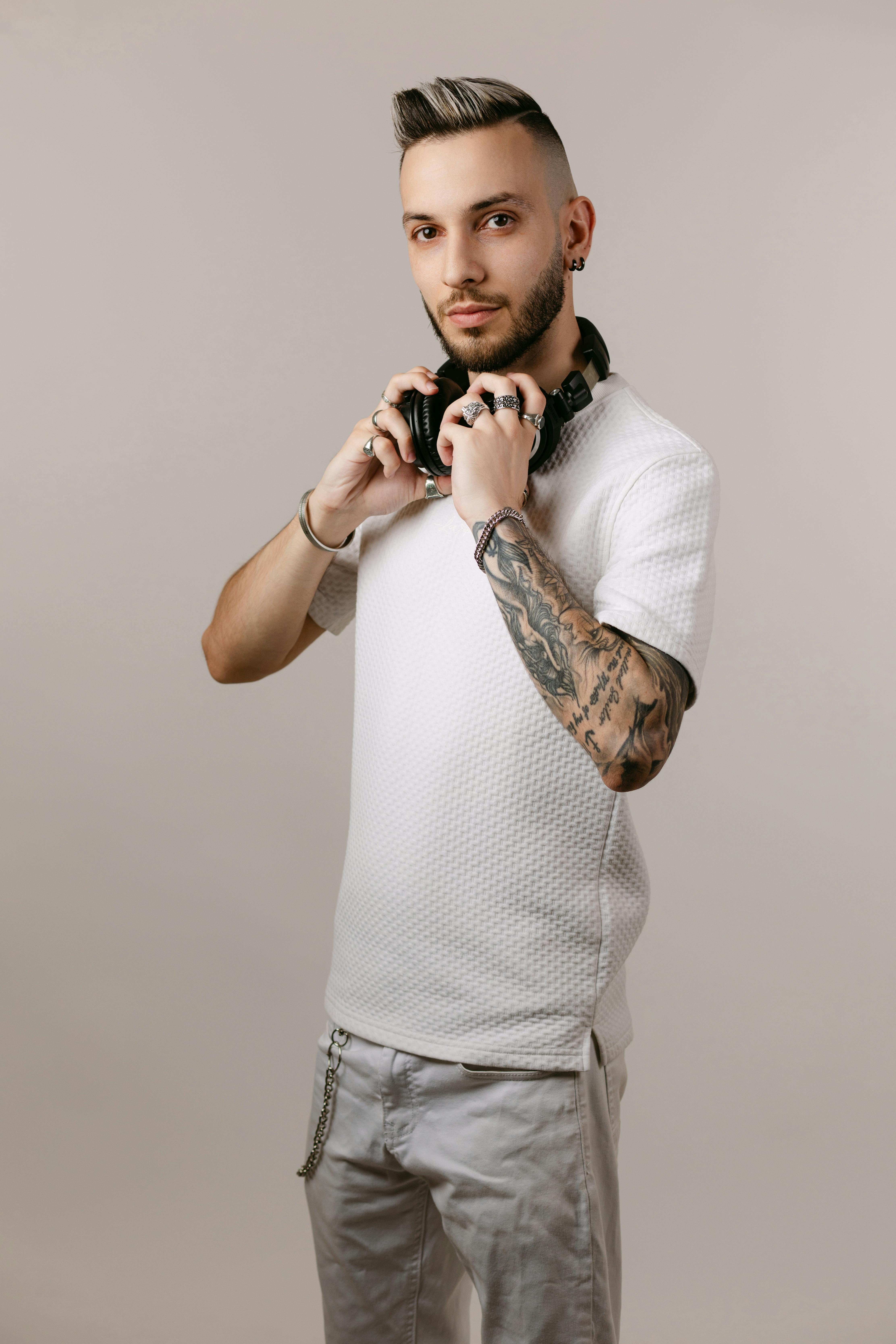 Ücretsiz Dövmeli ve kulaklıklı şık adam, nötr bir arka plana karşı kendinden emin bir şekilde poz veriyor. Stok Fotoğraflar