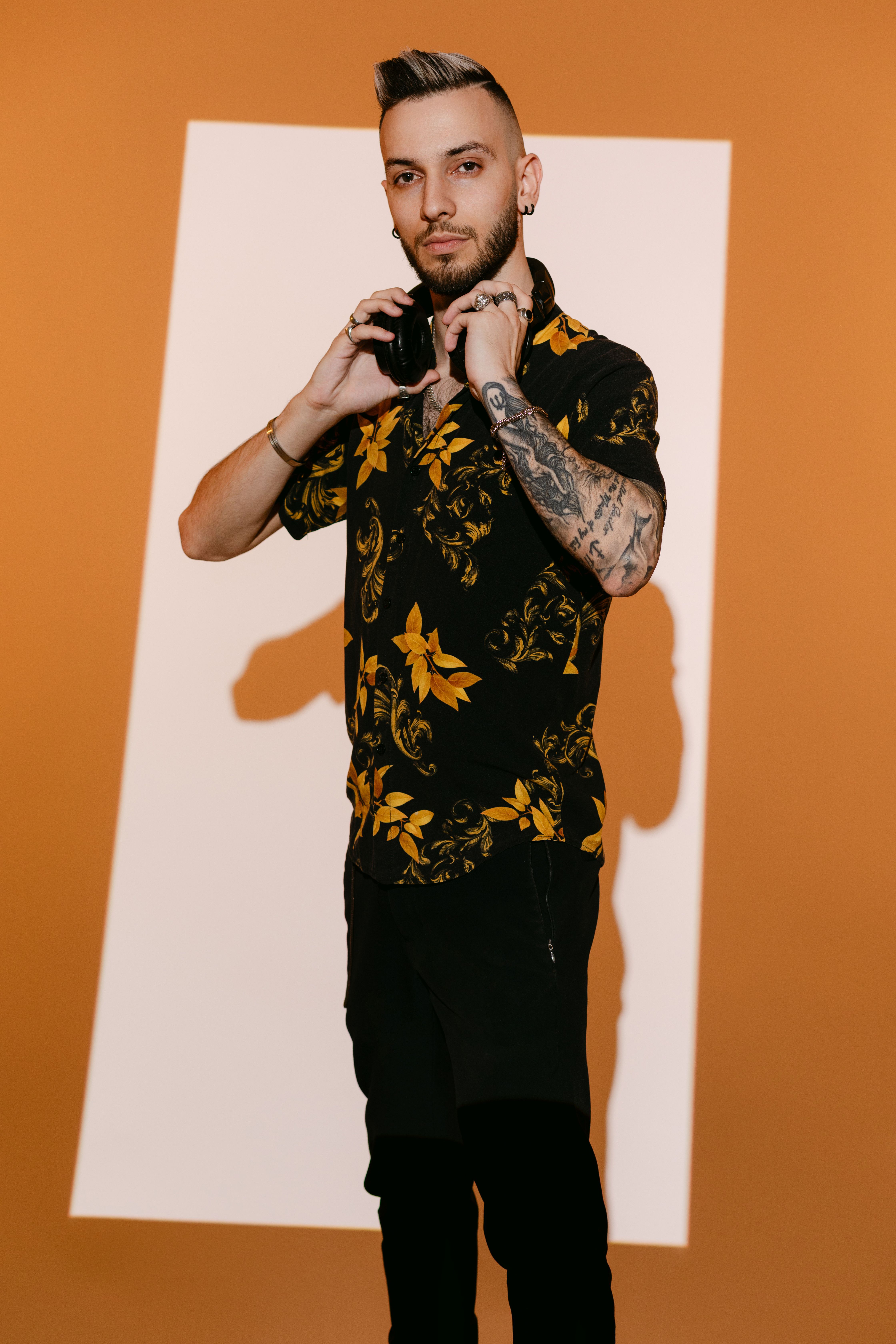 Fashionable DJ wearing floral shirt and headphones, posing confidently against geometric backdrop.