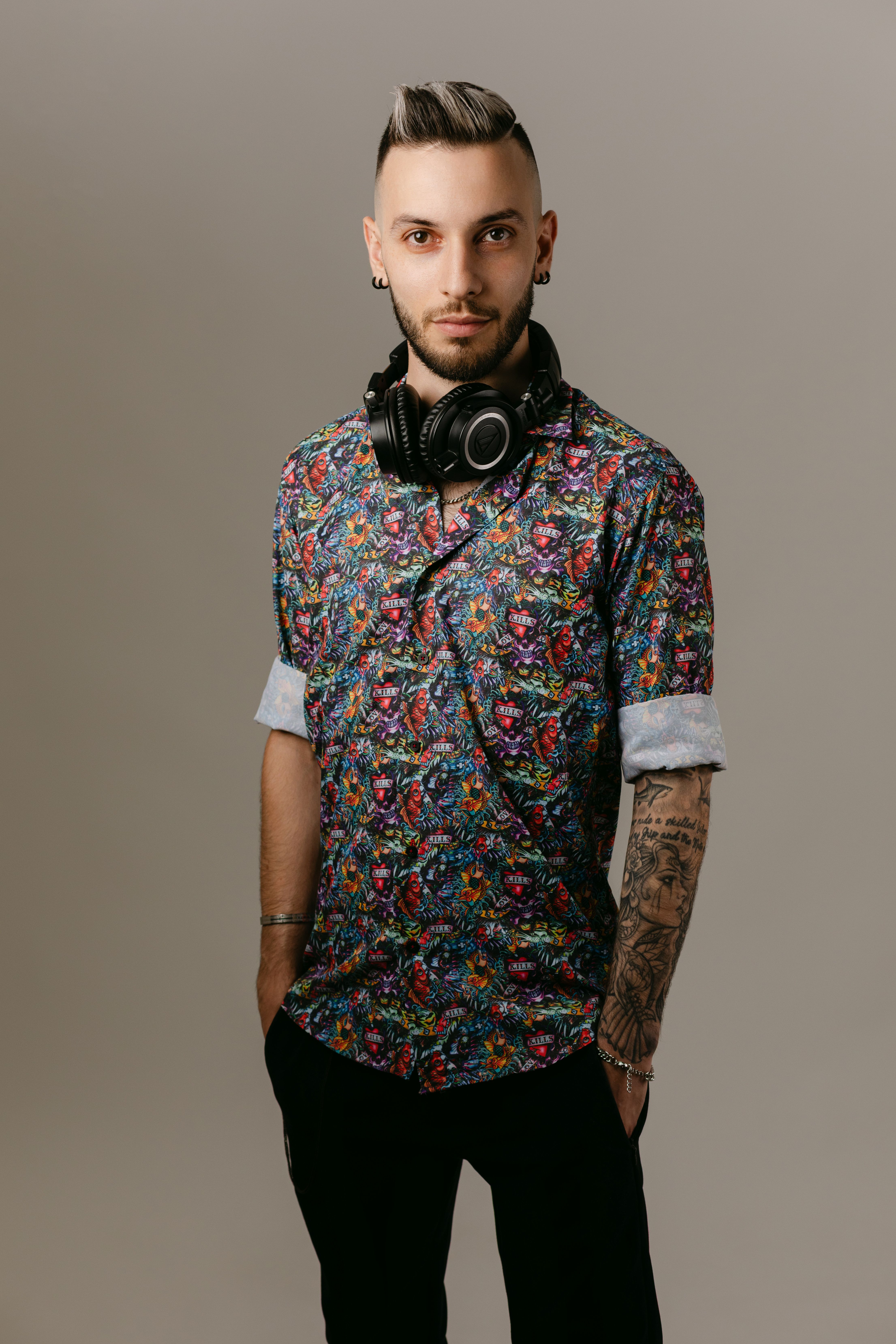Trendy young man with headphones, posing confidently in floral shirt. Modern style and fashion expression captured.
