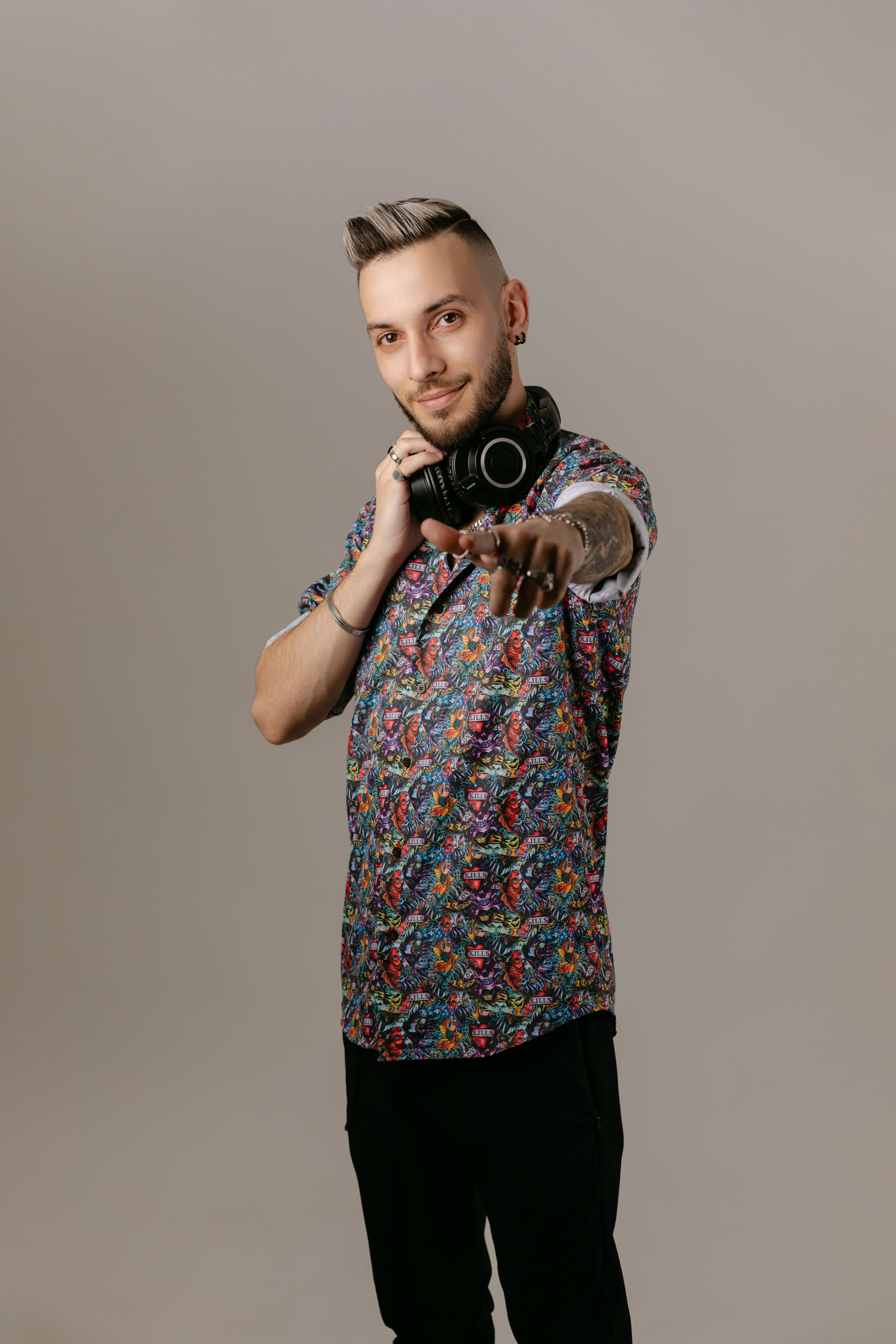 Stylish young DJ in floral shirt pointing with confidence and holding headphones