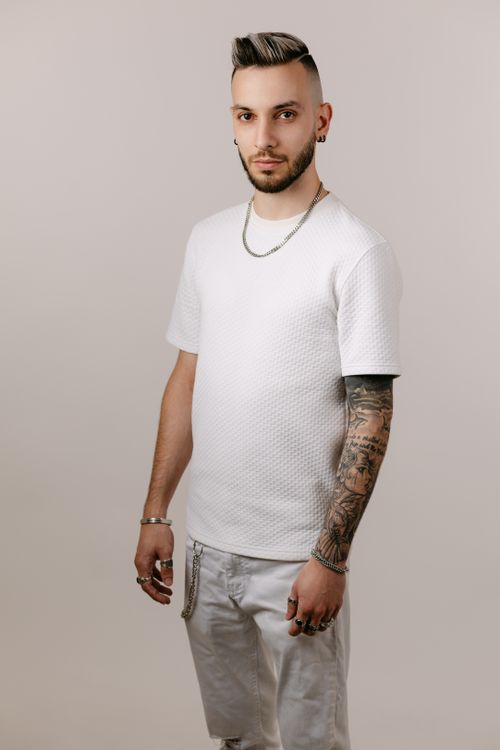 Free Stylish young adult male wearing white outfit and showcasing tattoos in a studio setting. Stock Photo