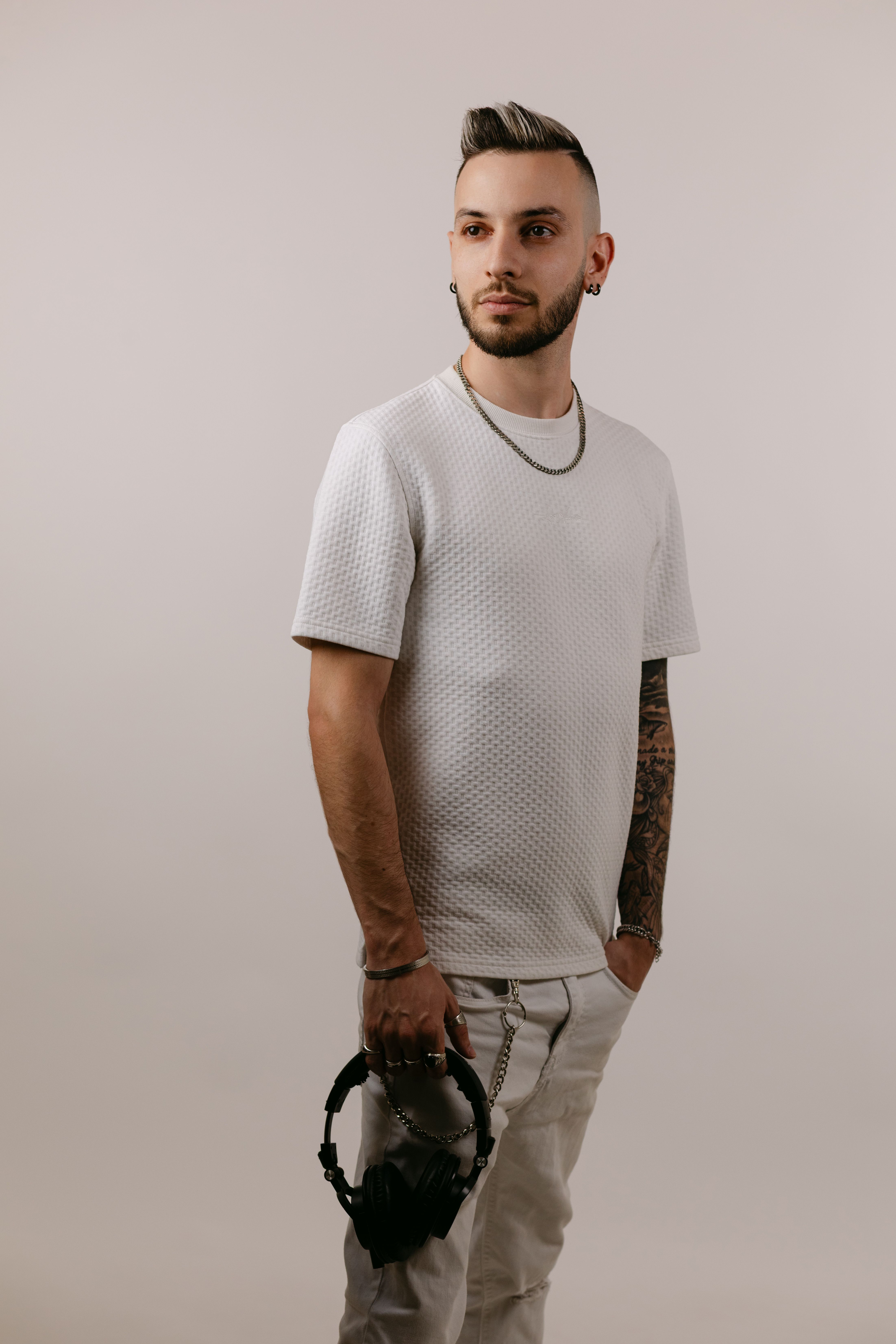 Portrait of a stylish young man holding headphones, wearing a white outfit in a studio.