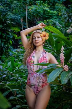 A woman in a floral swimsuit poses gracefully in a lush tropical garden showcasing vibrant plants.