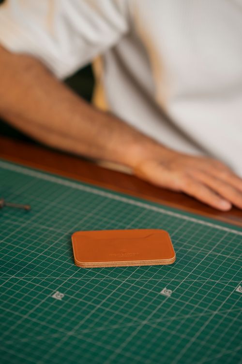 Free A handmade leather wallet rests on a crafting mat with blurred hands in the background. Stock Photo