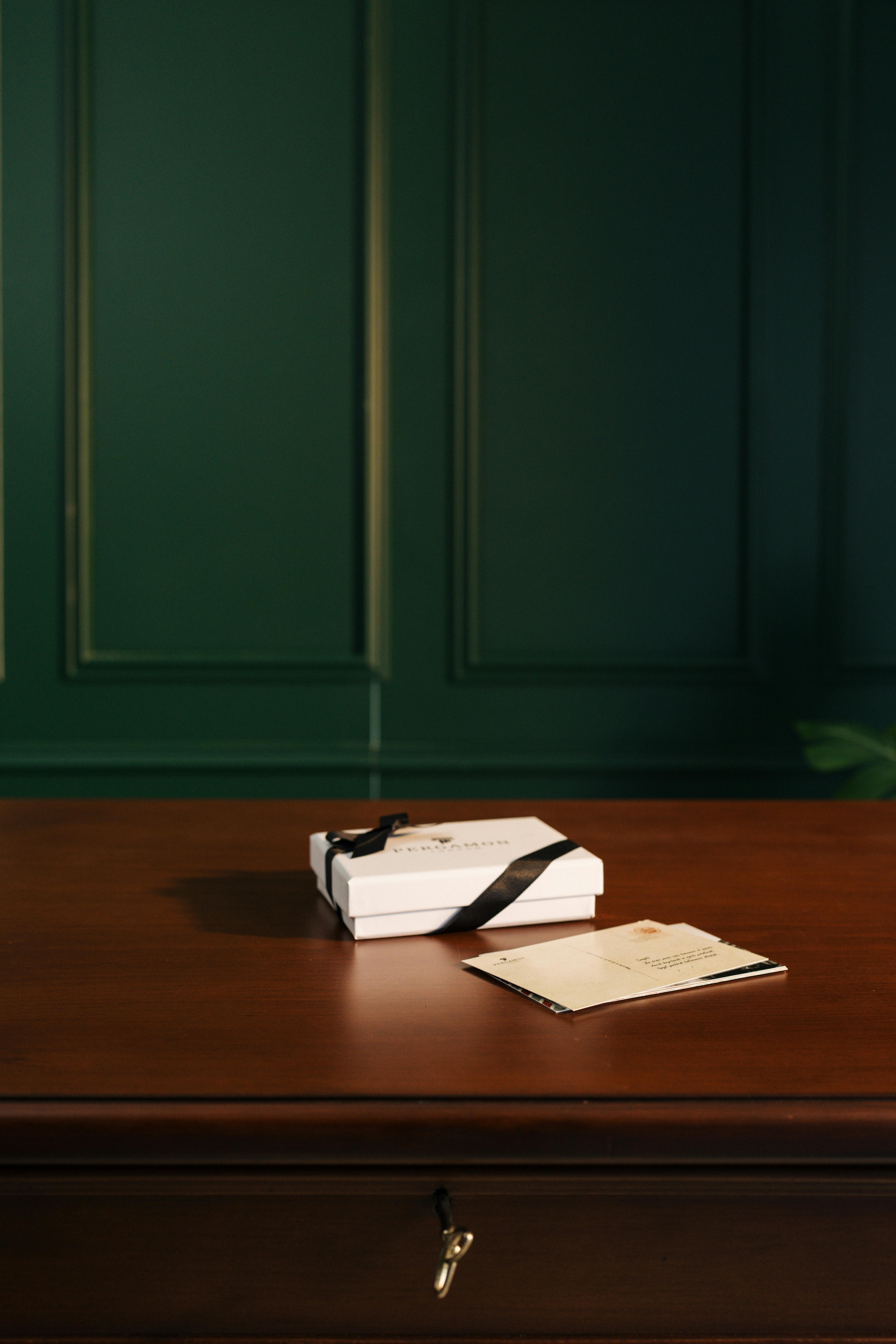 Zadarmo Biela darčeková krabička so stuhou sedí na drevenom stole pri zelenej obloženej stene a evokuje eleganciu. Fotka z fotobanky