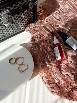 Chic flat lay featuring gold jewelry and beauty serums on sequined fabric, perfect for lifestyle concepts.