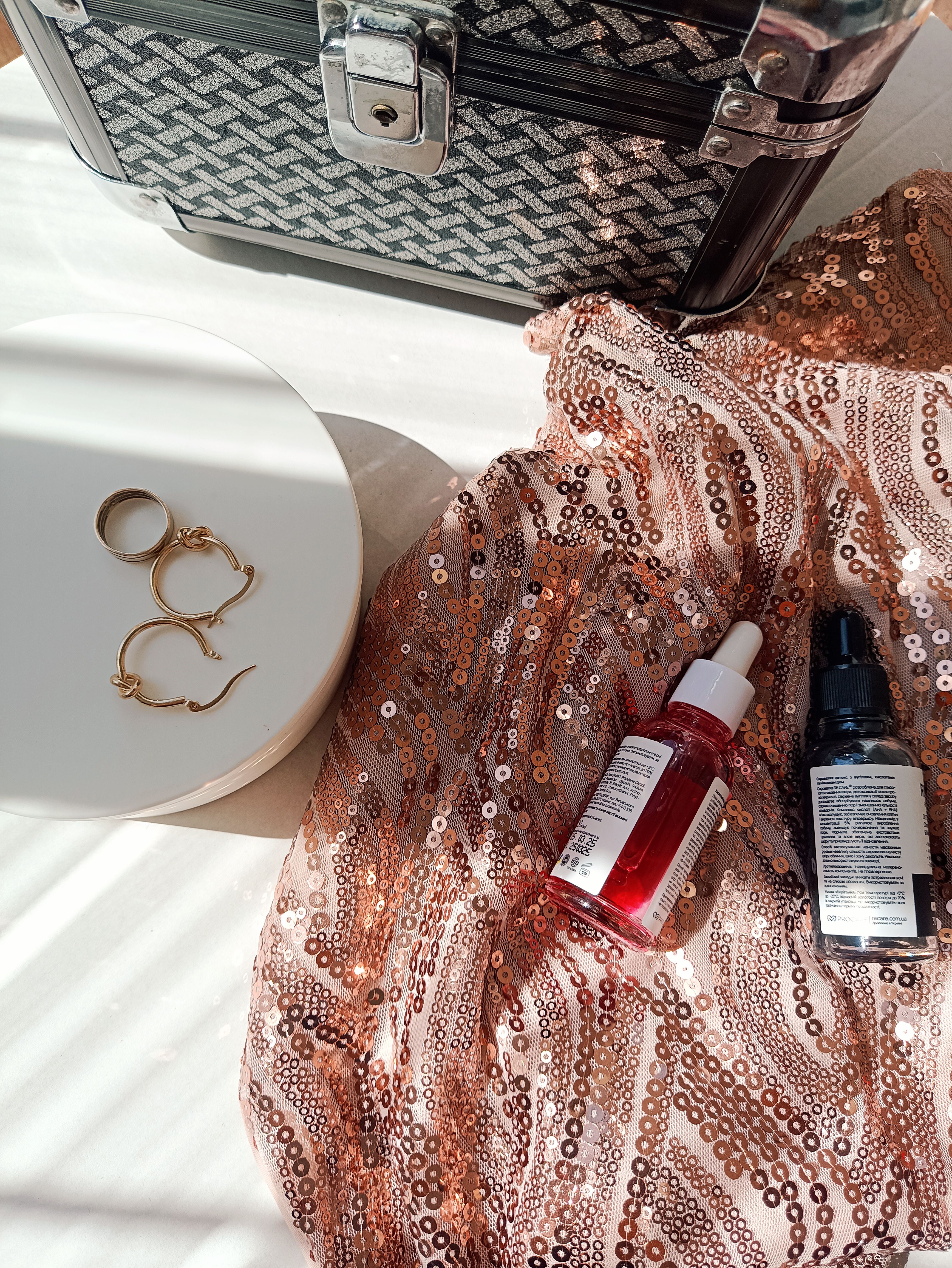 Beautiful flat lay showcasing skincare products and jewelry on a sequin fabric.