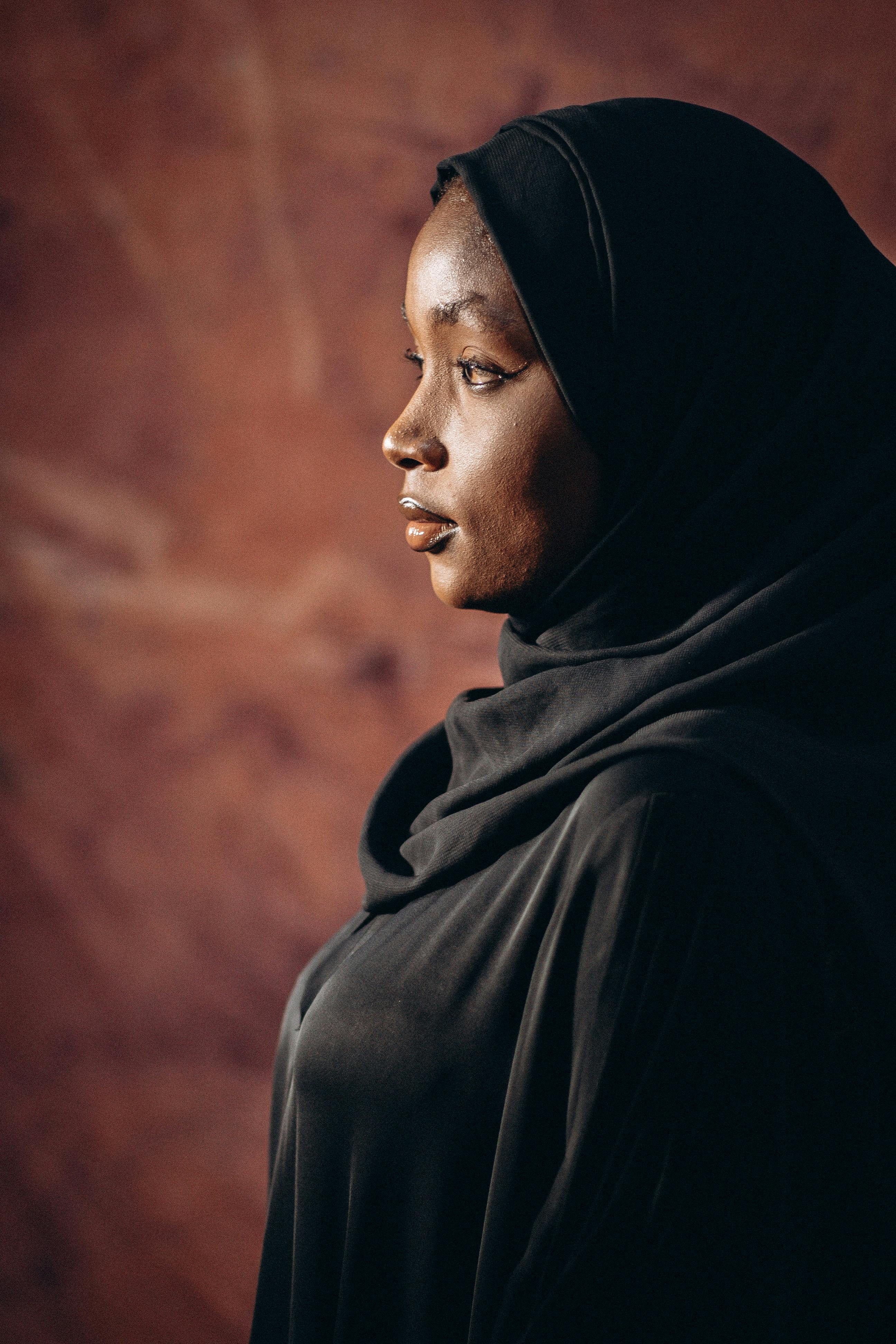 A beautiful side profile portrait of a woman wearing a hijab against a warm, textured backdrop.