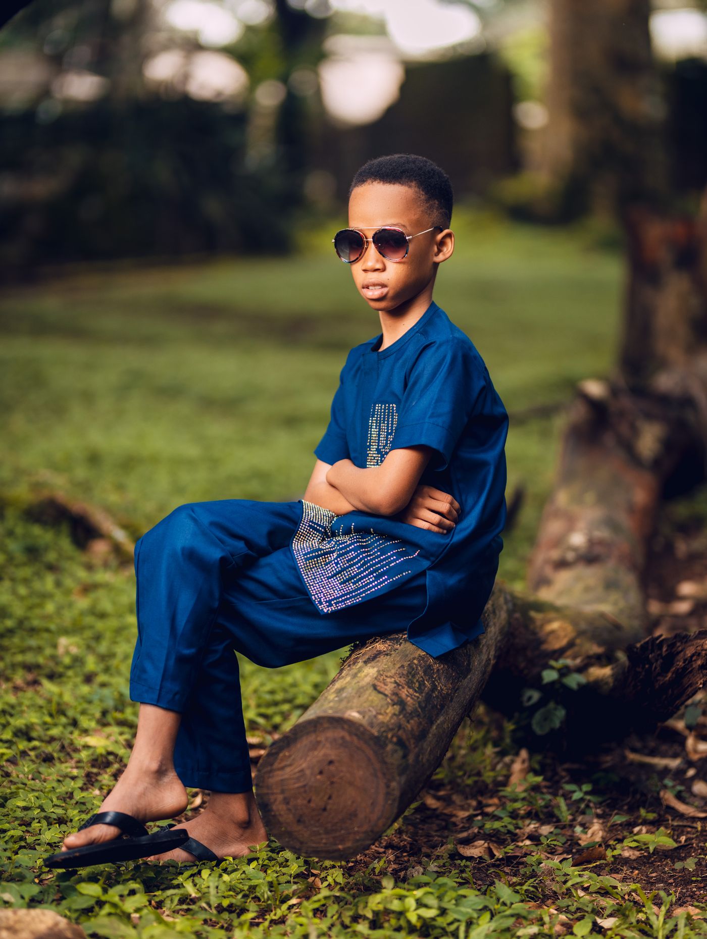 A boy in navy sits on a fallen log in a garden in Aburi, Eastern Region.