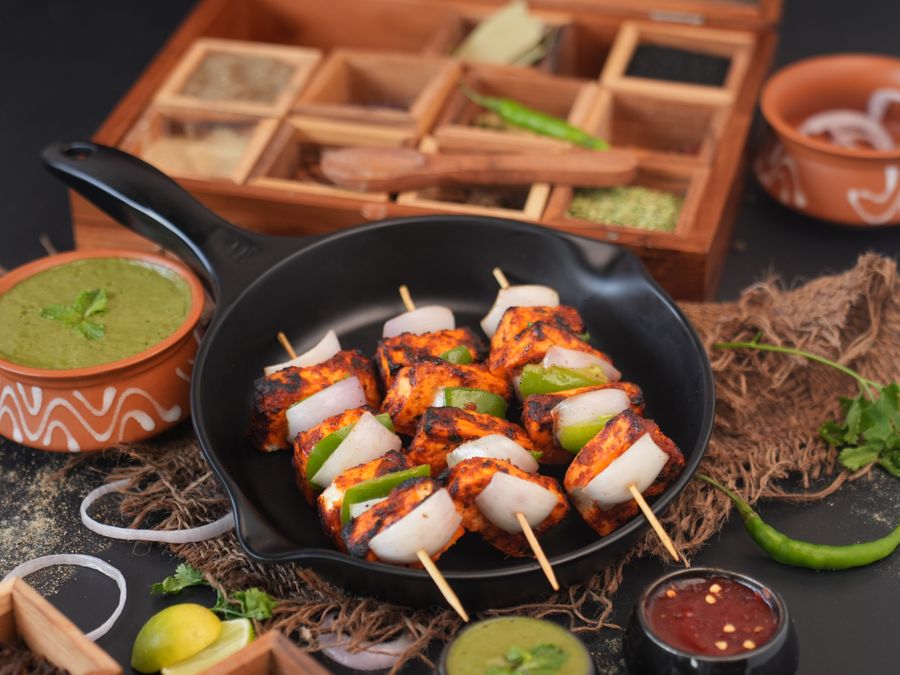 Grilled paneer tikka in skillet with chutneys and vibrant garnish