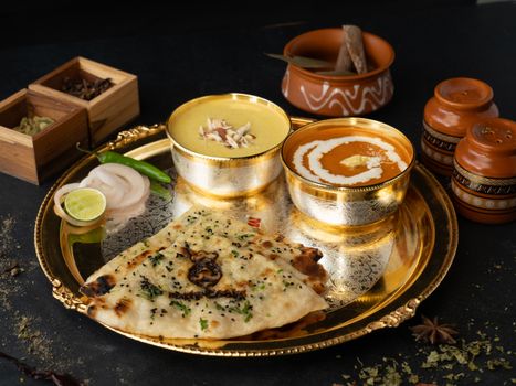 A delectable Indian thali featuring dal, butter chicken, and naan on a golden platter.