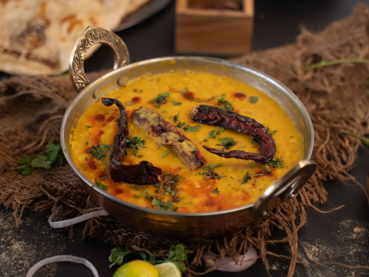 Golden yellow dal with fried dried red chilies and cilantro in a brass kadai