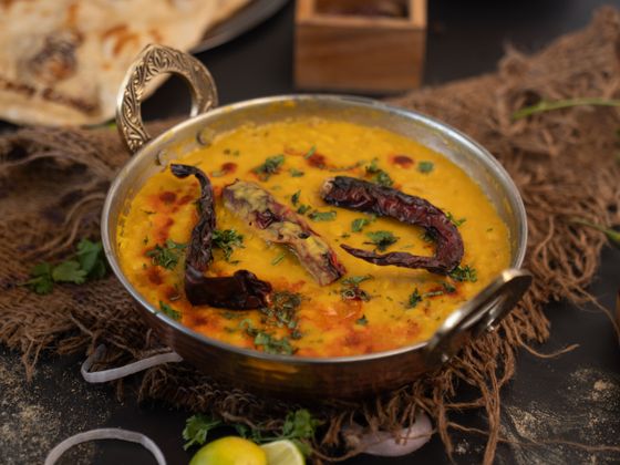 Golden yellow dal with fried dried red chilies and cilantro in a brass kadai