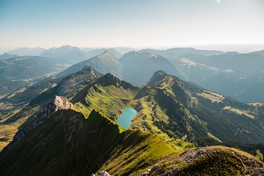 A breathtaking view of alpine mountains with lush valleys and a serene lake under a clear sky.