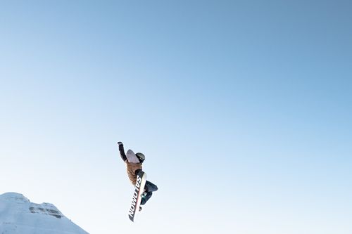 Free Snowboarder performing an aerial trick on a sunny winter day with a clear blue sky backdrop. Stock Photo
