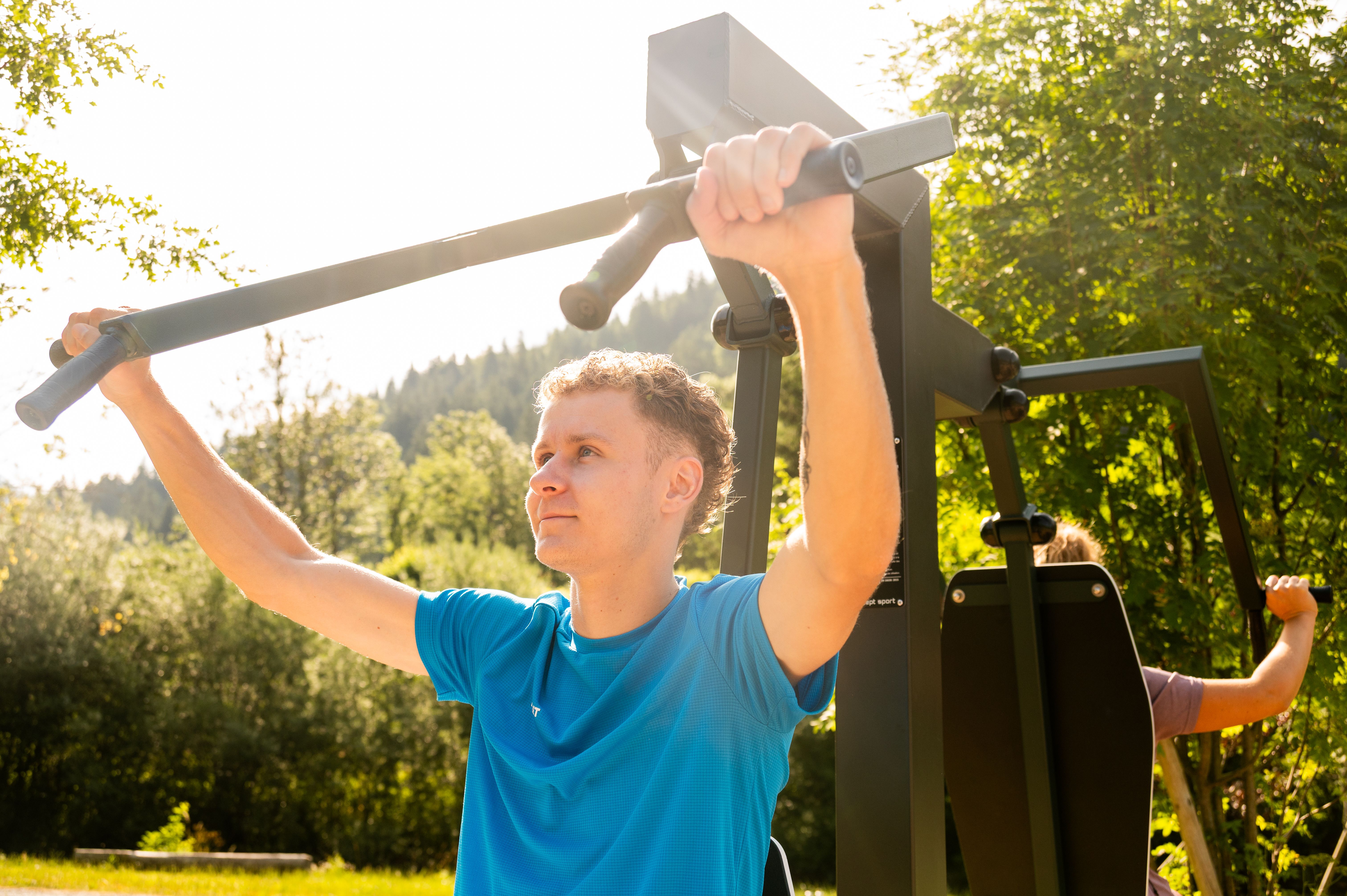 A man working out on outdoor fitness equipment on a sunny day in a park.