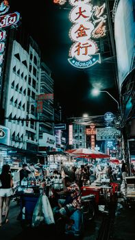 Explore the bustling night street market with vibrant signs and busy vendors in Bangkok.