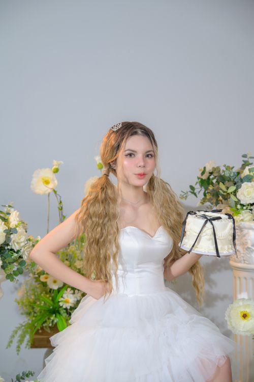 Free Young woman in a white dress holding a cake in a floral setting. Stock Photo