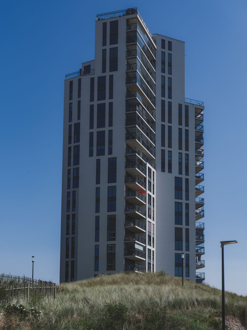 Een hoog, modern appartementengebouw met balkons onder een strakblauwe hemel in Almere.