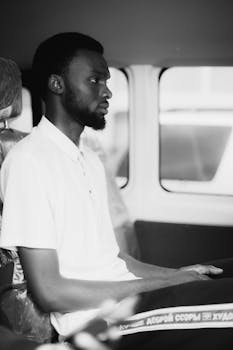 Black and white portrait of a thoughtful young man sitting in a vehicle.