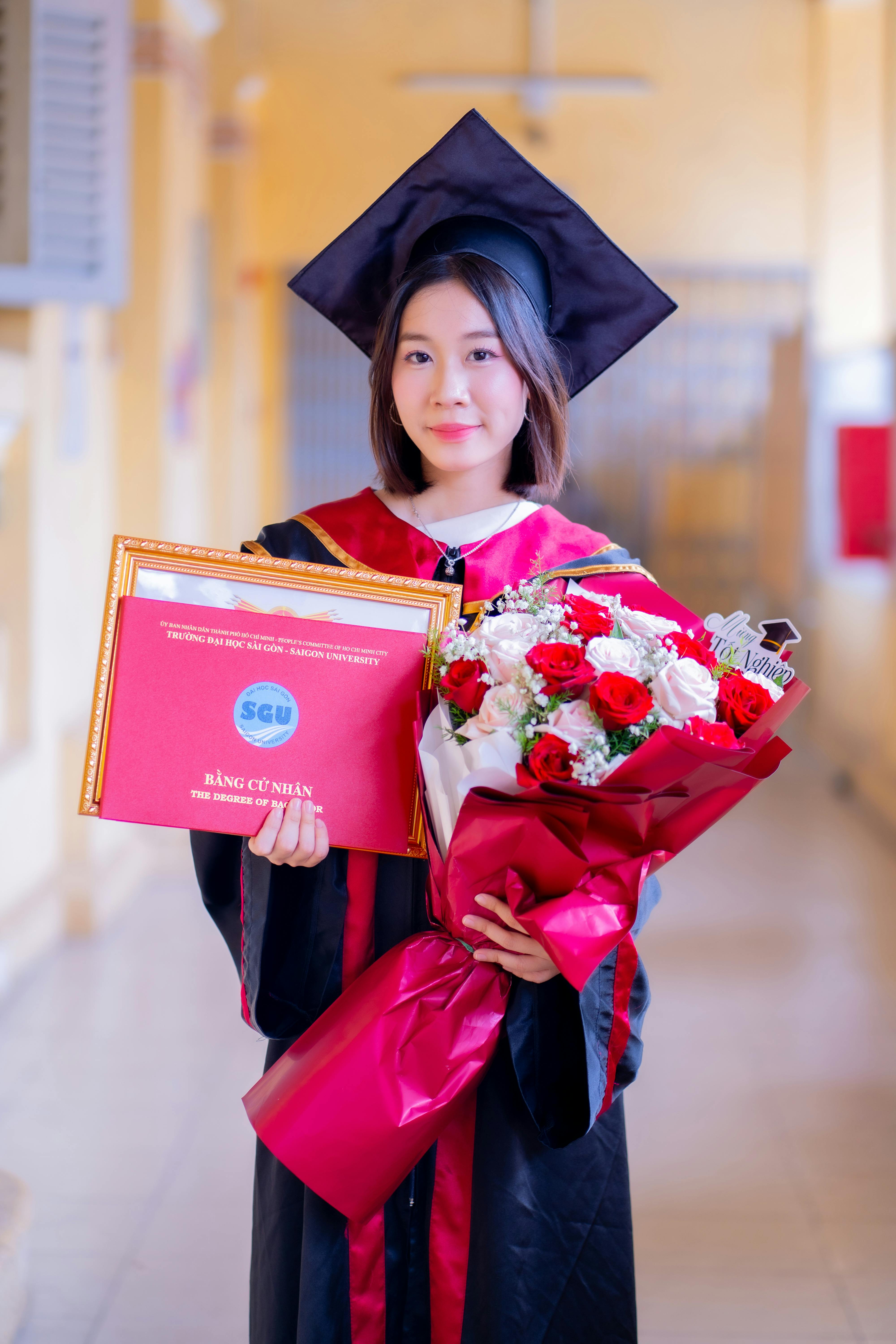 A proud young graduate holds her degree and a bouquet in a hallway, embodying academic success and celebration.