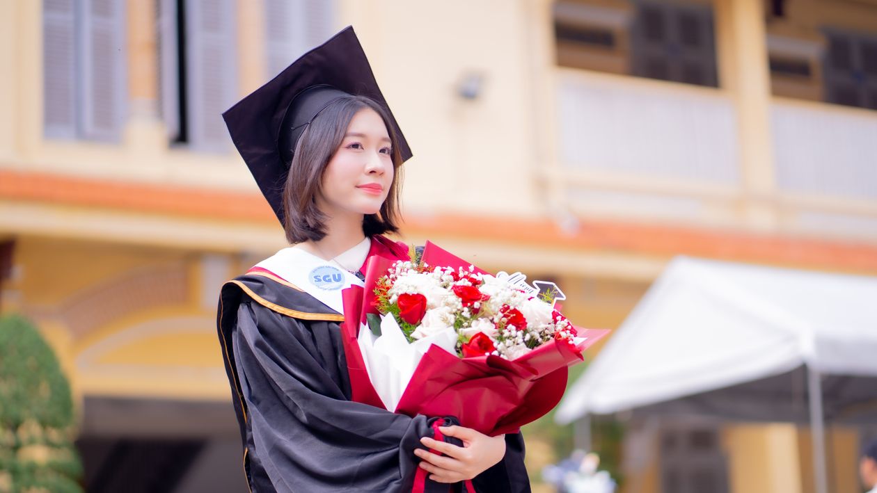 Young graduate holding flowers on campus after college commencement ceremony