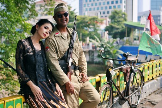 A couple in vintage military attire posing beside a classic bicycle outdoors.