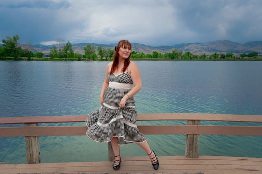 A woman in a gingham summer dress poses by a serene mountain lake in Boulder, Colorado.