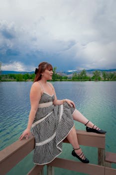 Woman in a gingham dress sitting on a pier by a scenic lake in Boulder, Colorado, with a mountainous backdrop.
