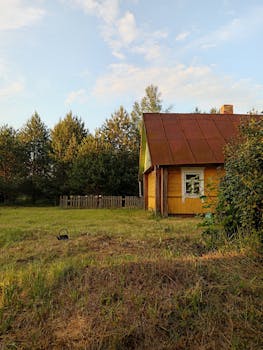 Charming wooden cabin with rusty metal roof in a serene rural landscape, surrounded by trees.