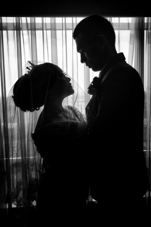 Free Romantic silhouette of a bride and groom embracing by window. Perfect for wedding themes. Stock Photo
