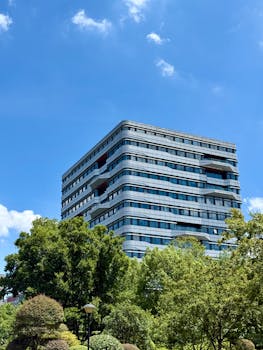 A contemporary high-rise building in Shanghai, surrounded by lush greenery under a clear blue sky.