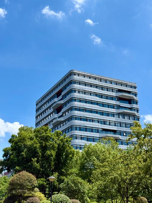 Free A contemporary high-rise building in Shanghai, surrounded by lush greenery under a clear blue sky. Stock Photo