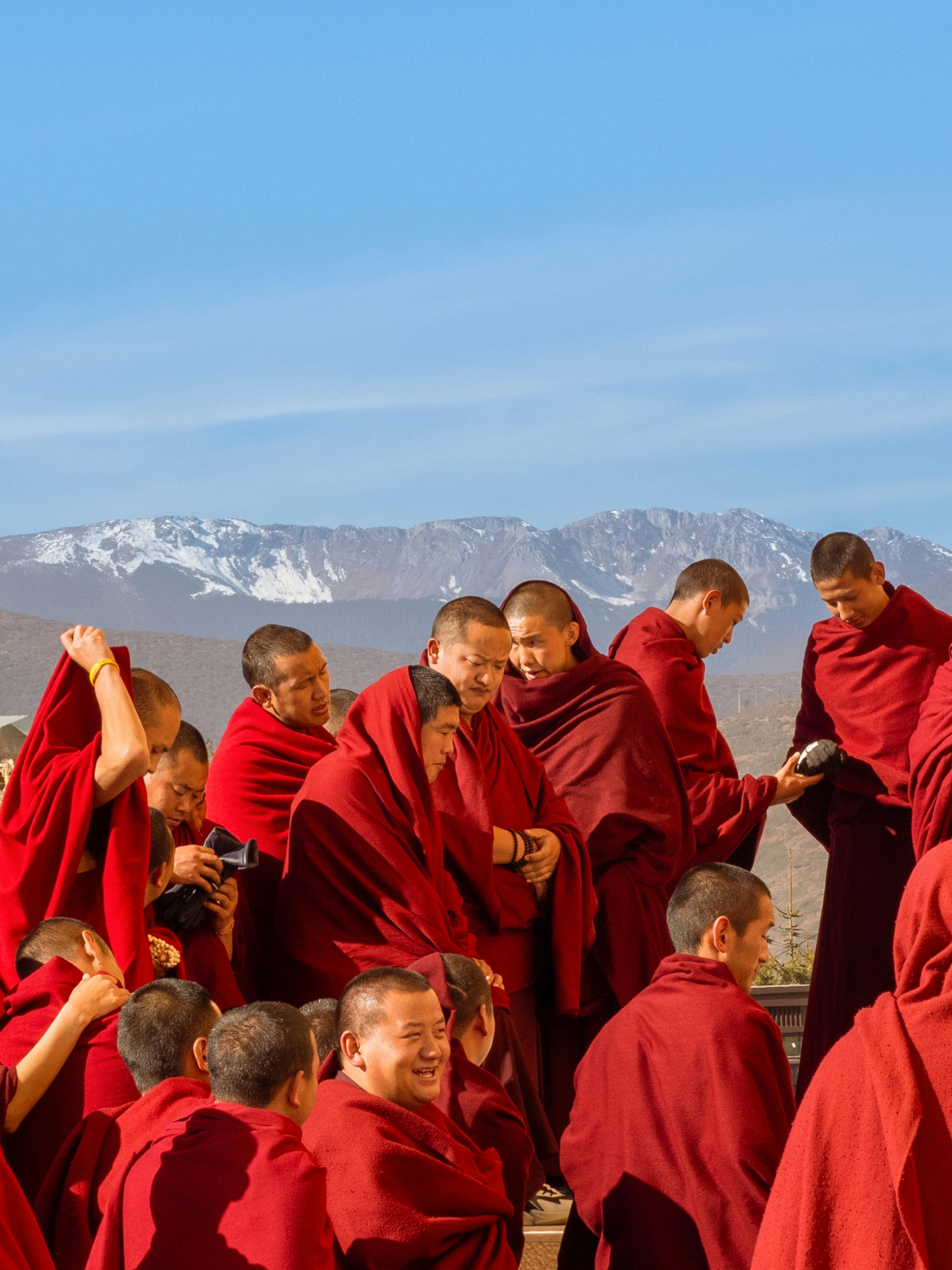 A group of monks in red robes outdoors with snowy mountains. Captured during daylight.