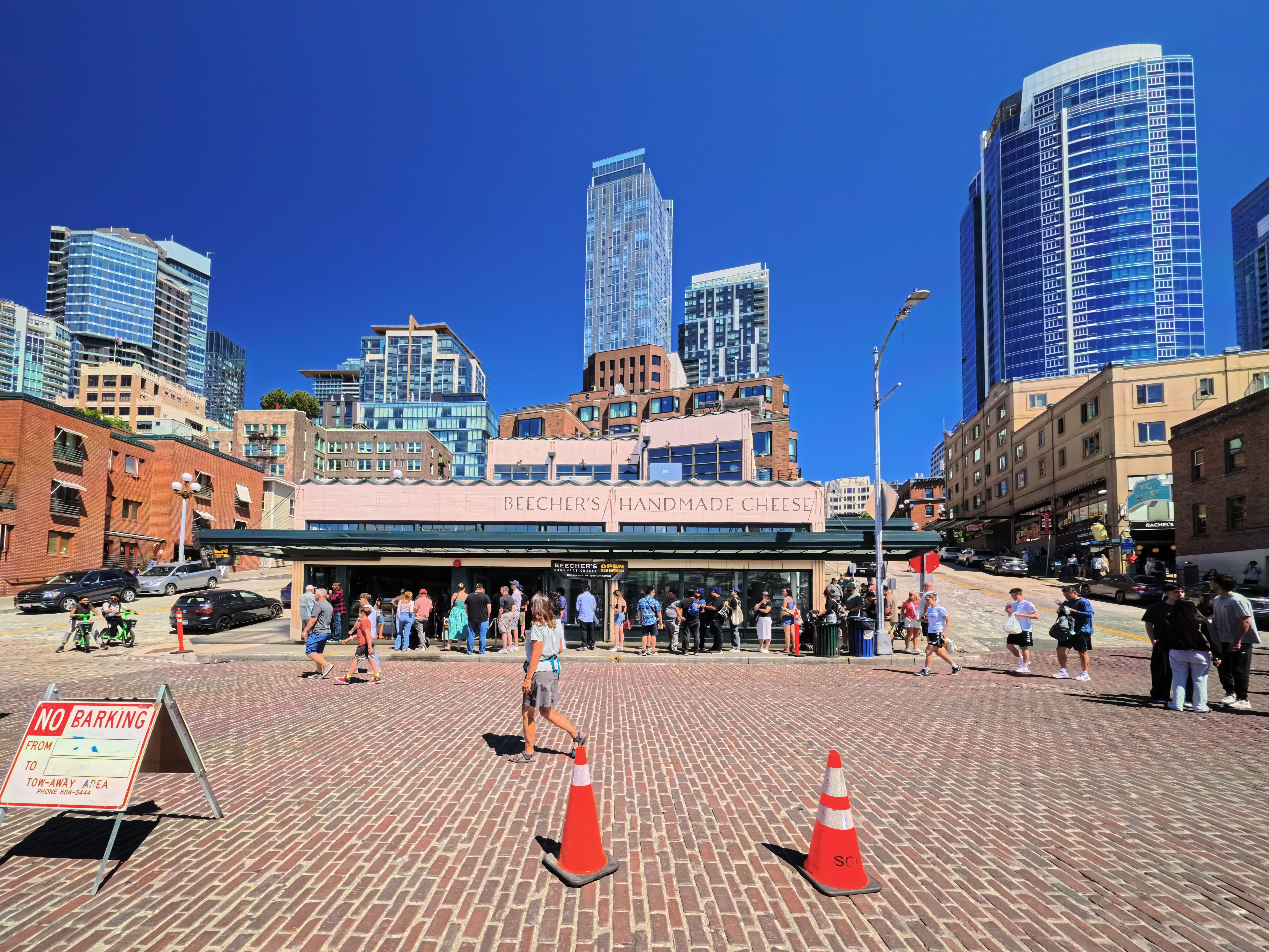 People walking near Beecher's Handmade Cheese near Pike Place Market, Seattle, with city skyscrapers.
