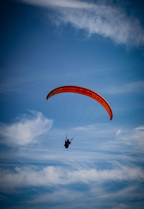 Free A paraglider with an orange canopy flying high under a bright blue sky with scattered clouds. Stock Photo