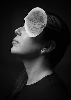Black and white portrait of a woman with a large leaf covering one eye, creating an artistic and unique composition.