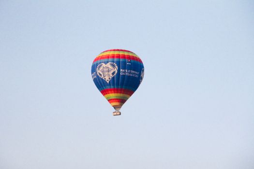 Vibrant hot air balloon flying high against a clear blue sky.