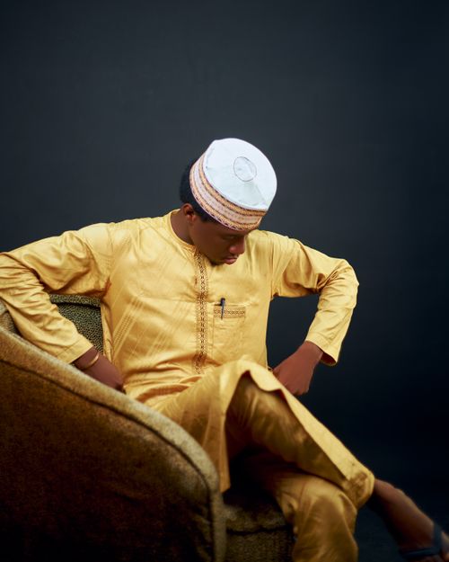 Free Man in golden traditional clothing seated on a chair against a dark background, deep in thought. Stock Photo