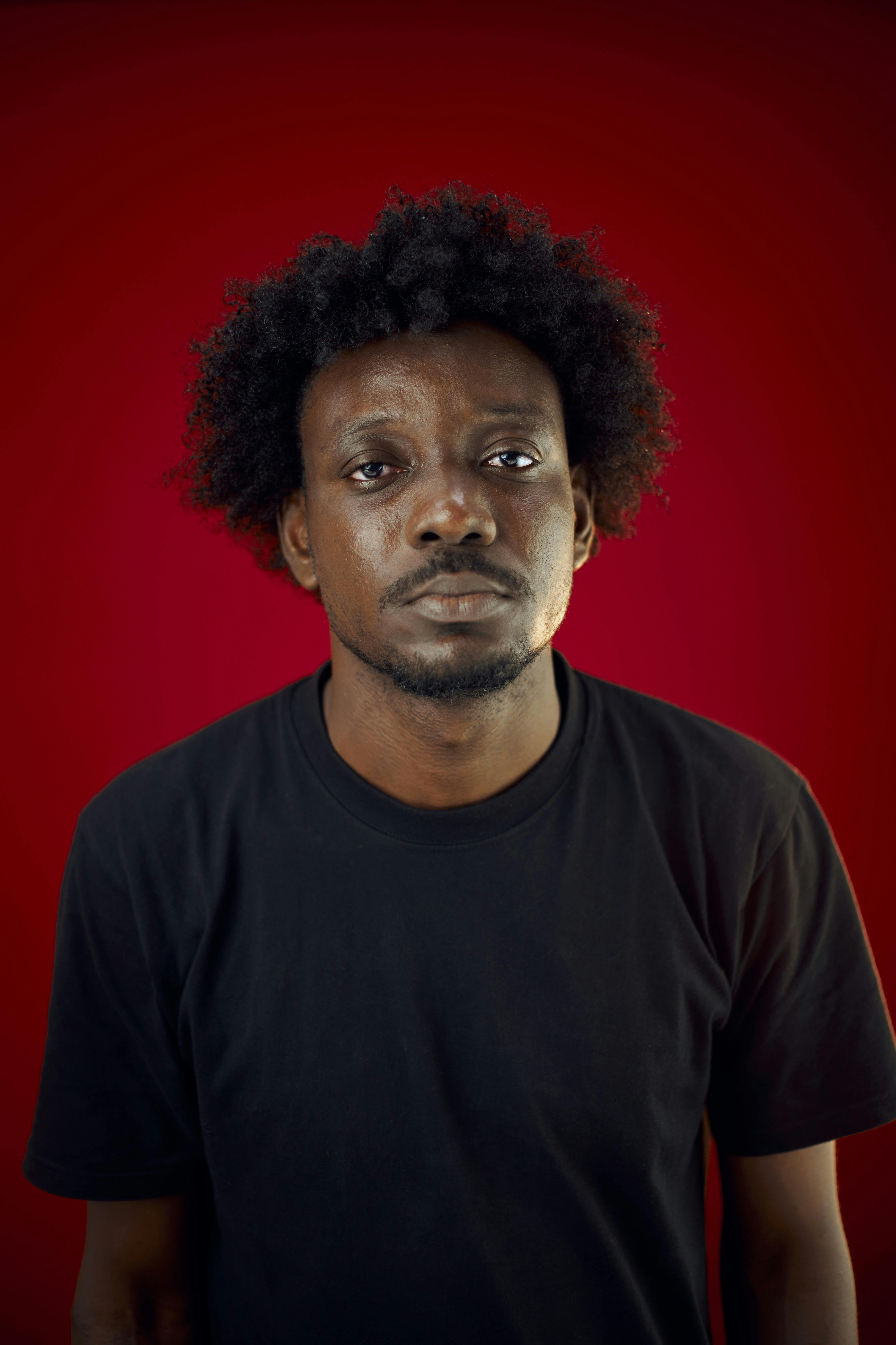 Close-up portrait of a man with afro hair against a bright red background.