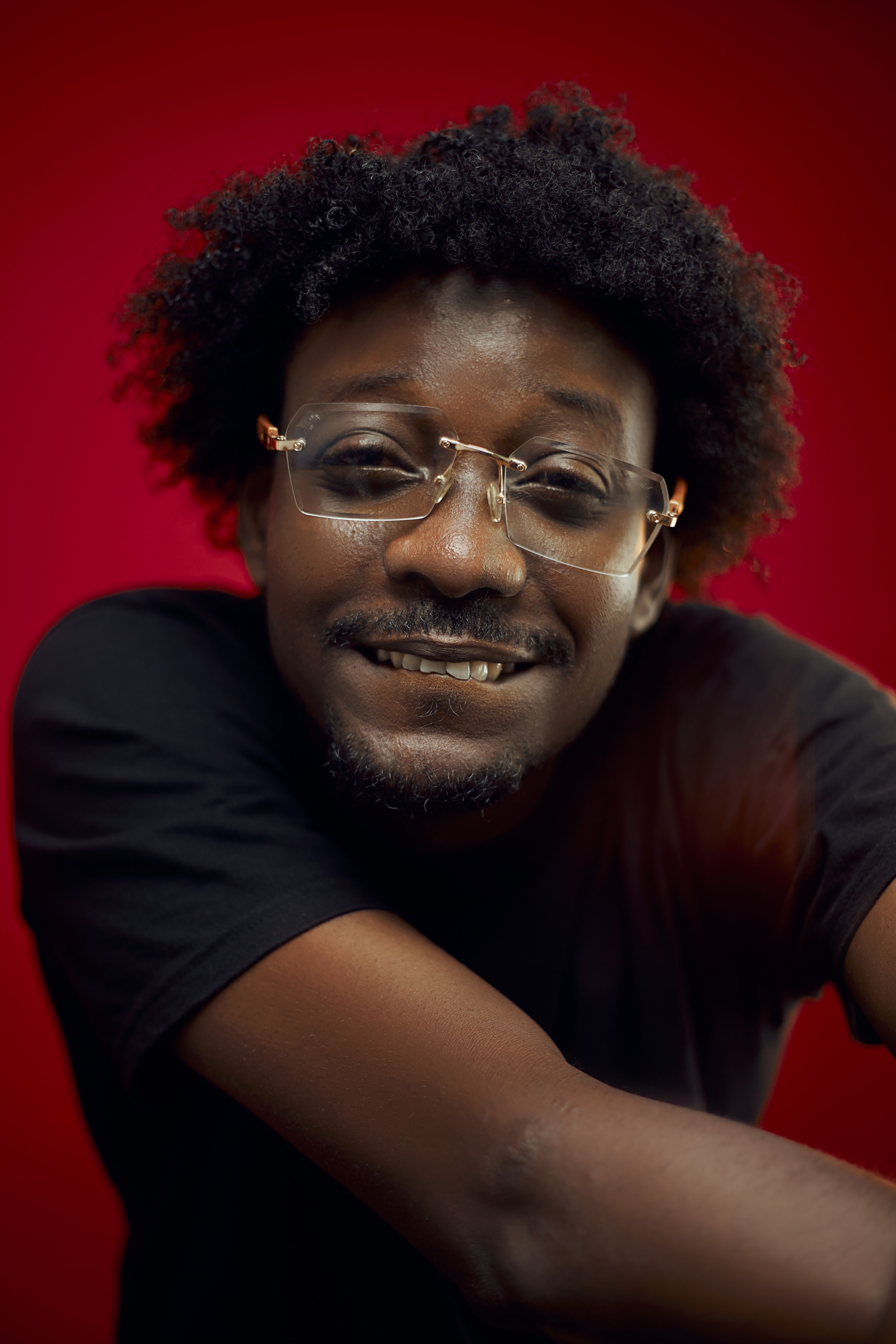 Close-up portrait of a smiling man in glasses against a vibrant red background.