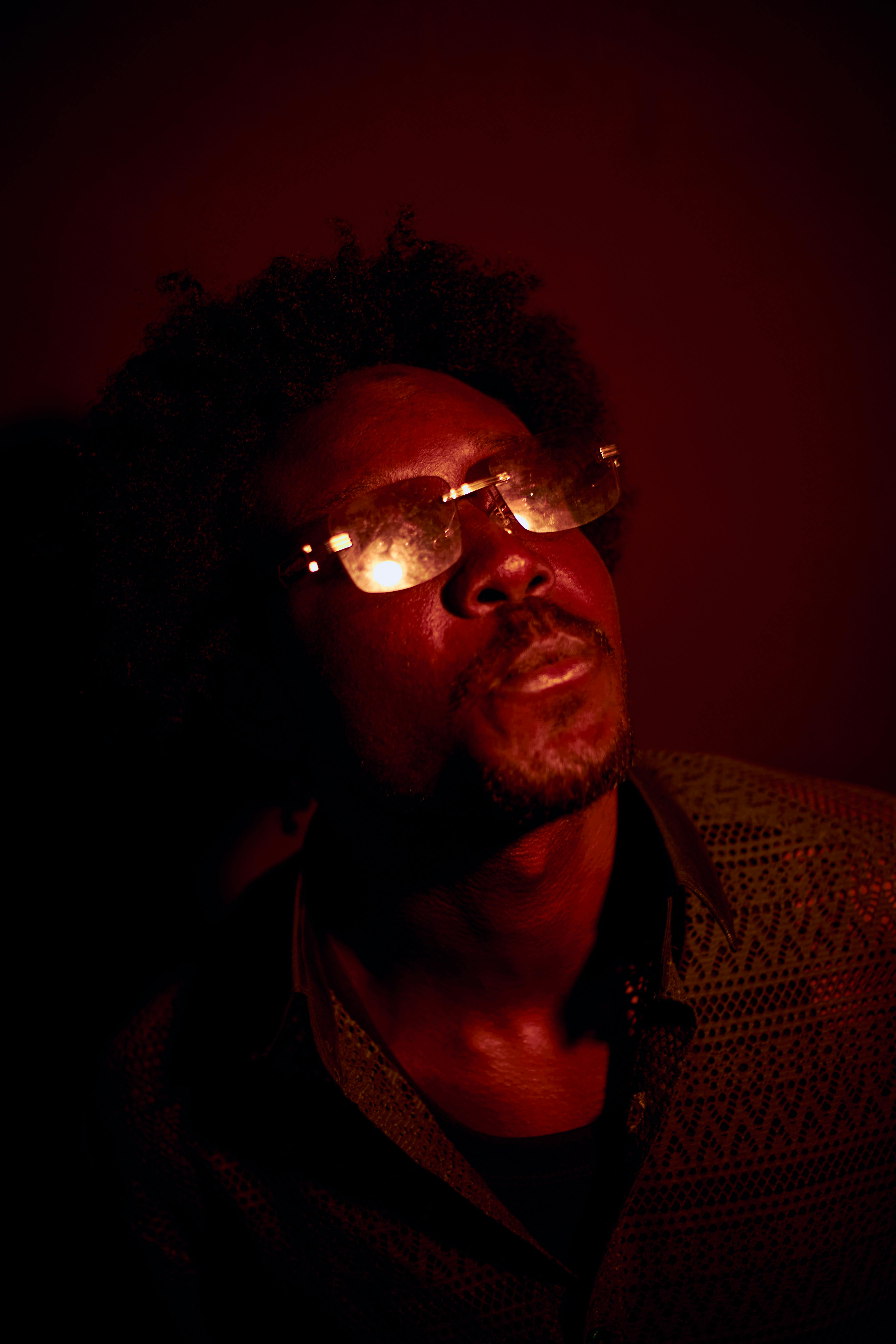A dramatic portrait of a man in reflective glasses with a moody red lighting.