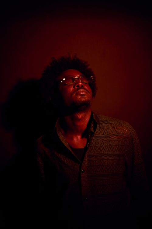 Free A man in glasses gazes upward, bathed in red and shadowy lighting, creating a dramatic mood. Stock Photo