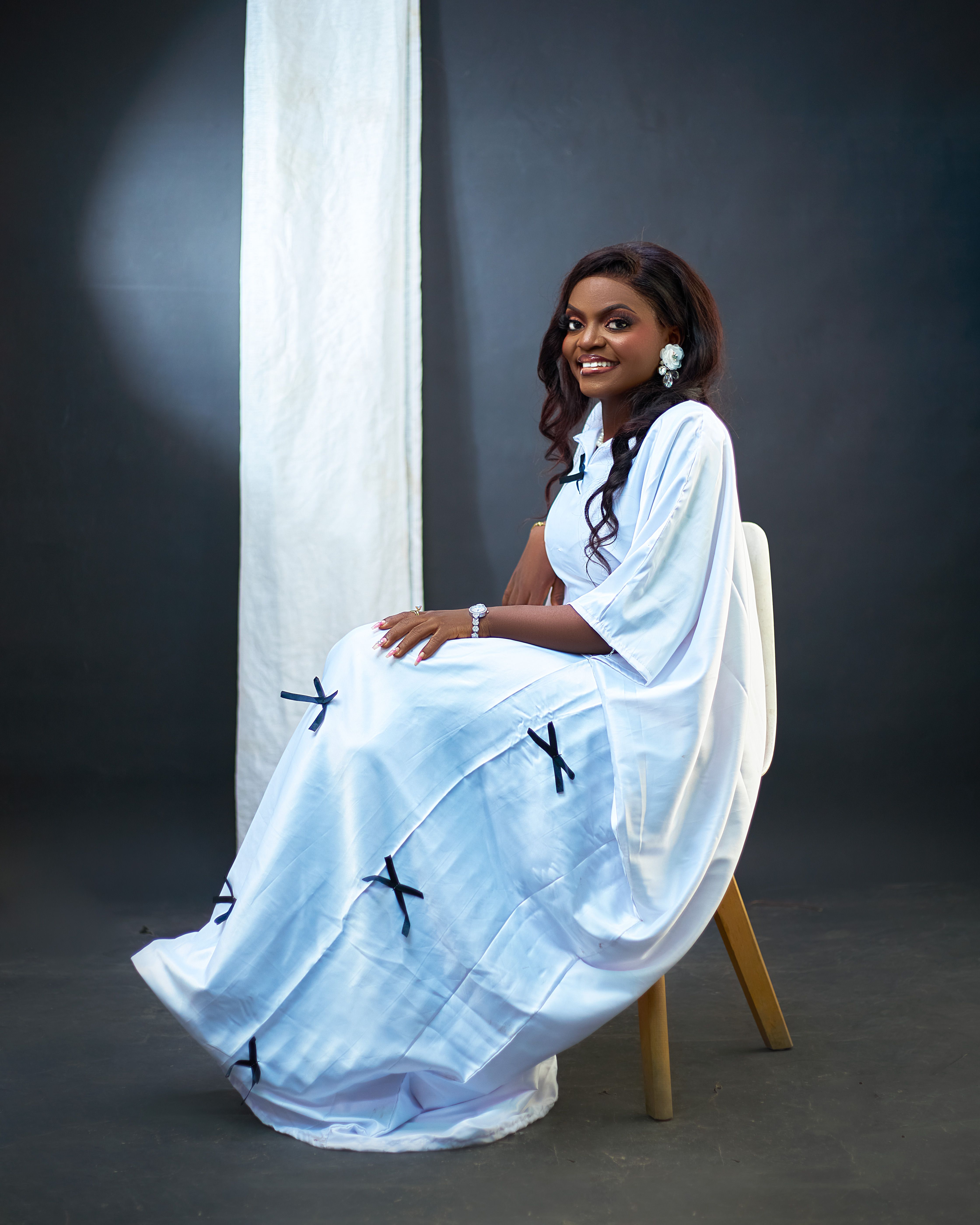 Portrait of a smiling woman in white traditional attire seated indoors.